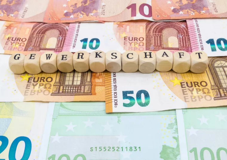 Auf verschiedenen Geldnoten sind Würfel mit Buchstaben aufgereiht. Die Würfel bilden das Wort "Gewerkschaft".