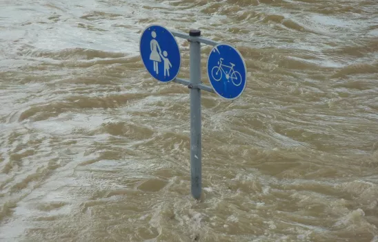 Wassermassen, die ein Verkehrsschild überfluten, das einen Fußgänger- und einen Radweg anzeigt Wassermassen, die ein Verkehrsschild überfluten, das einen Fußgänger- und einen Radweg anzeigt