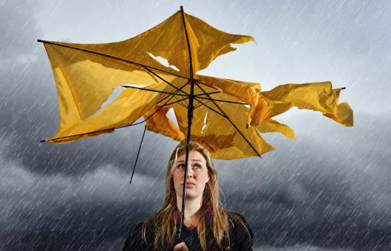 Eine Frau steht im Regen unter grauen Wolken unter einem zerrissenen gelben Regenschirm und blickt hinauf. Eine Frau steht im Regen unter grauen Wolken unter einem zerrissenen gelben Regenschirm und blickt hinauf.