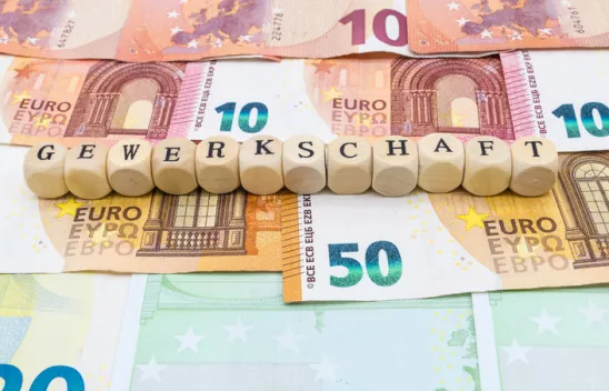 Auf verschiedenen Geldnoten sind Würfel mit Buchstaben aufgereiht. Die Würfel bilden das Wort "Gewerkschaft". Auf verschiedenen Geldnoten sind Würfel mit Buchstaben aufgereiht. Die Würfel bilden das Wort "Gewerkschaft".