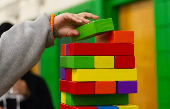 Buntes Jenga-Spiel, bei dem eine Kinderhand einen Stein nach oben legt.