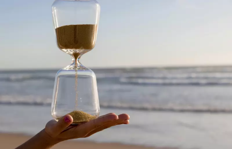 Eine Hand hält eine Sanduhr. Im Hintergrund sieht man Strand und Meer. Eine Hand hält eine Sanduhr. Im Hintergrund sieht man Strand und Meer.