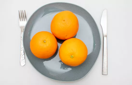 Drei Orangen auf einem Teller, rechts und links davon liegen Messer und Gabel. Drei Orangen auf einem Teller, rechts und links davon liegen Messer und Gabel.