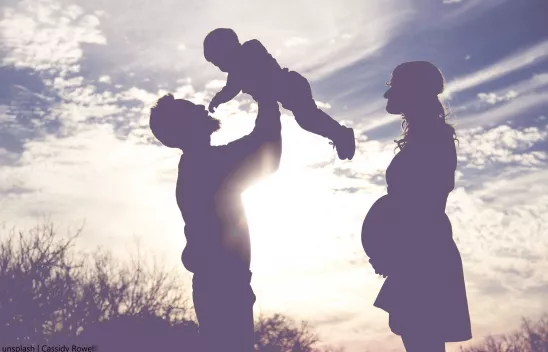 Die Silhouette einer Familie mit Kleinkind im Gegenlicht der Sonne auf einem Feld. Die Silhouette einer Familie mit Kleinkind im Gegenlicht der Sonne auf einem Feld.