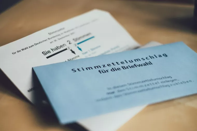 Ein aufgeklappter Stimmzettelbrief, auf dem ein blauer Stimmzettelumschlag für die Briefwahl liegt.