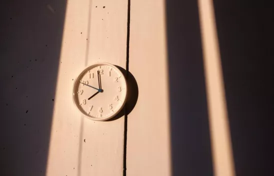 Eine weiße, analoge Wanduhr im Licht der Sonne.