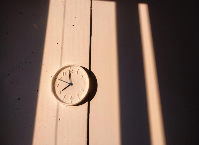 Eine weiße, analoge Wanduhr im Licht der Sonne