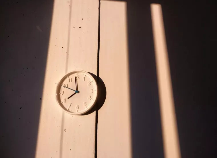 Eine weiße, analoge Wanduhr im Licht der Sonne