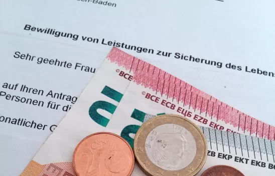 Ein Brief, auf dem "Bewilligung von Leistungen zur Sicherung des Lebens..." zu lesen ist, darauf liegen Münzen und Scheine Ein Brief, auf dem "Bewilligung von Leistungen zur Sicherung des Lebens..." zu lesen ist, darauf liegen Münzen und Scheine