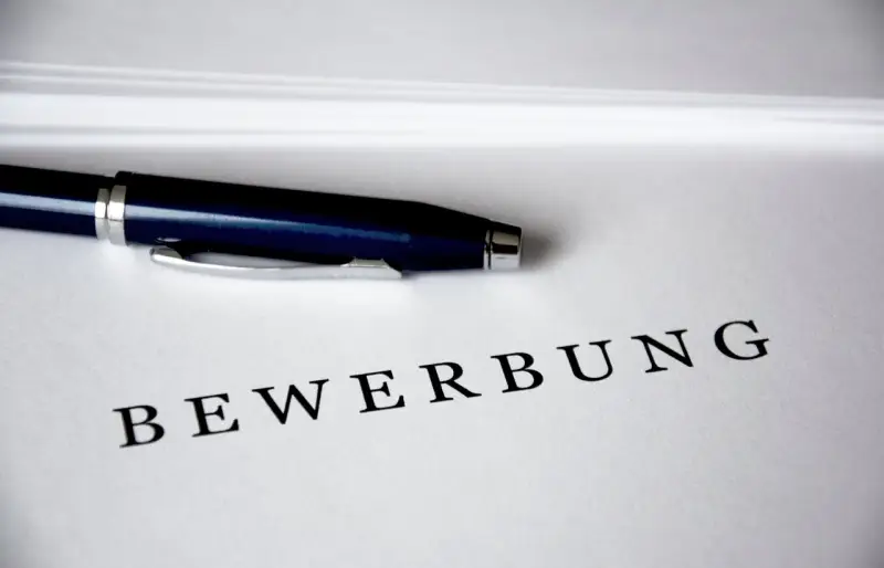 Schriftzug "Bewerbung" auf einem Blatt Papier, darüber liegt ein Kugelschreiber Schriftzug "Bewerbung" auf einem Blatt Papier, darüber liegt ein Kugelschreiber