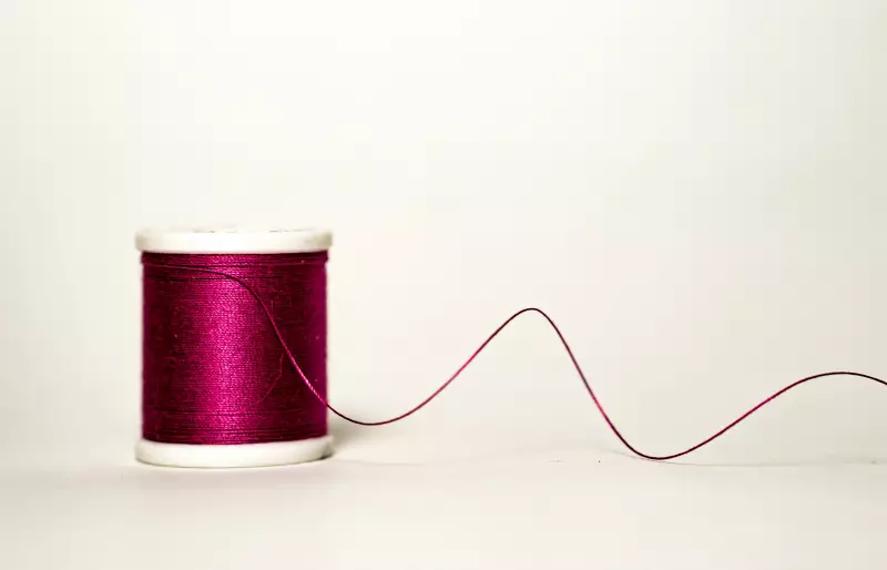 Eine Garnrolle, von der sich ein dunkelroter Faden abrollt. Eine Garnrolle, von der sich ein dunkelroter Faden abrollt.