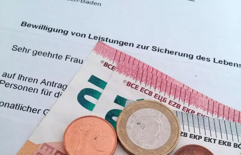 Euro-Münzen und Geldscheine liegen auf einem Bescheid zur Bewilligung von Sozialleistungen.