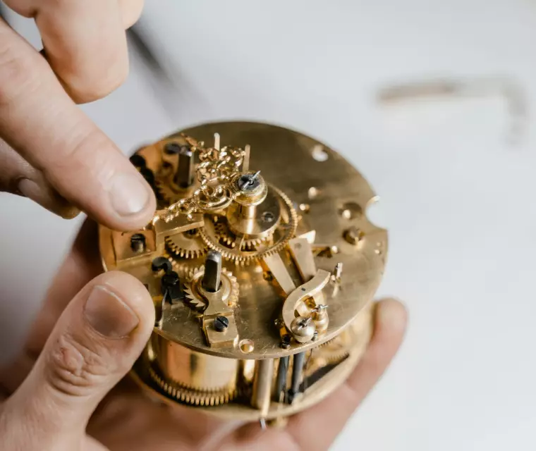 Hände arbeiten an einem Uhrwerk.