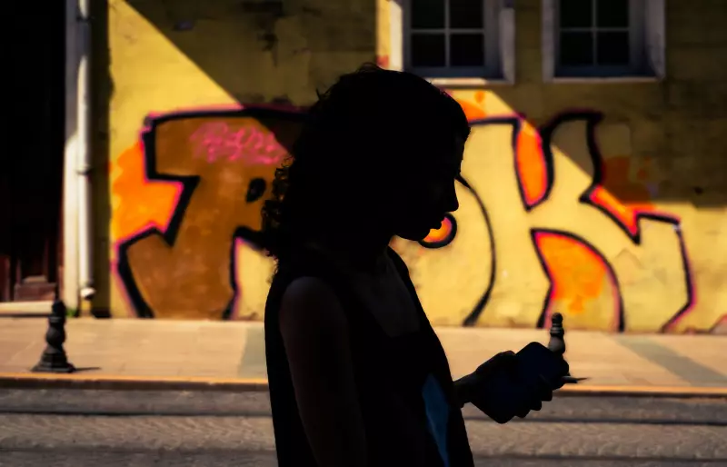 Die Silhouette einer Person, die auf ihr Smartphone schaut, vor einer Wand mit einem bunten Graffiti.