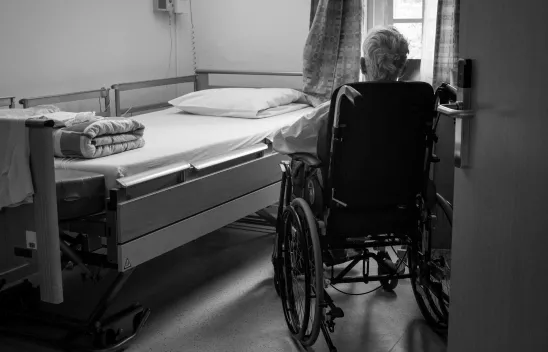 Pflegebedürftige Person im Rollstuhl vor Pflegebett.