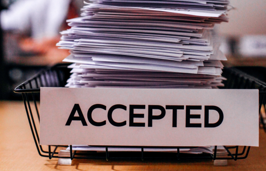 Ein Stapel Papier liegt in einem Korb, der mit dem Wort "ACCEPTED" beschriftet ist