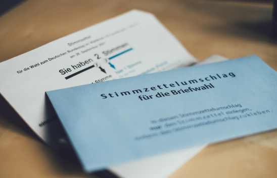 Ein aufgeklappter Stimmzettelbrief, auf dem ein blauer Stimmzettelumschlag für die Briefwahl liegt.