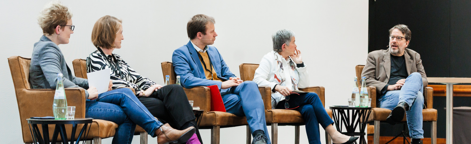 Blick auf eine Bühne, auf der sechs Personen auf dem Podium sitzen