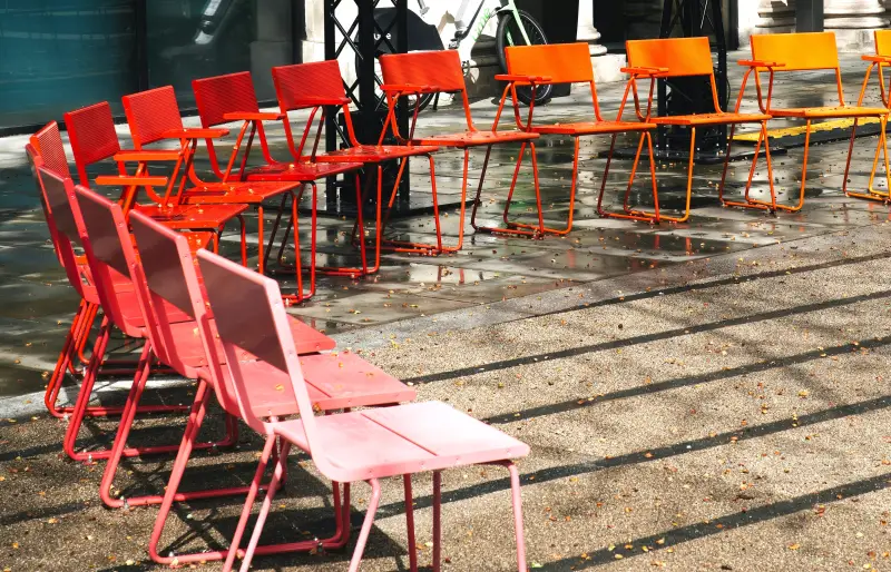Stühle in den Farben gelb, orange und rot, stehen im Halbkreis auf einem öffentlichen Platz. Stühle in den Farben gelb, orange und rot, stehen im Halbkreis auf einem öffentlichen Platz.