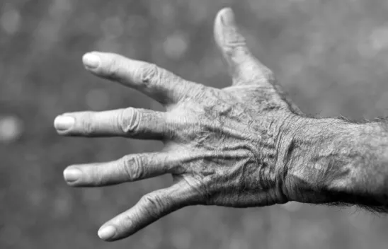 Nahaufnahme einer alten, faltigen Hand mit ausgestreckten Fingern in Schwarzweiß.