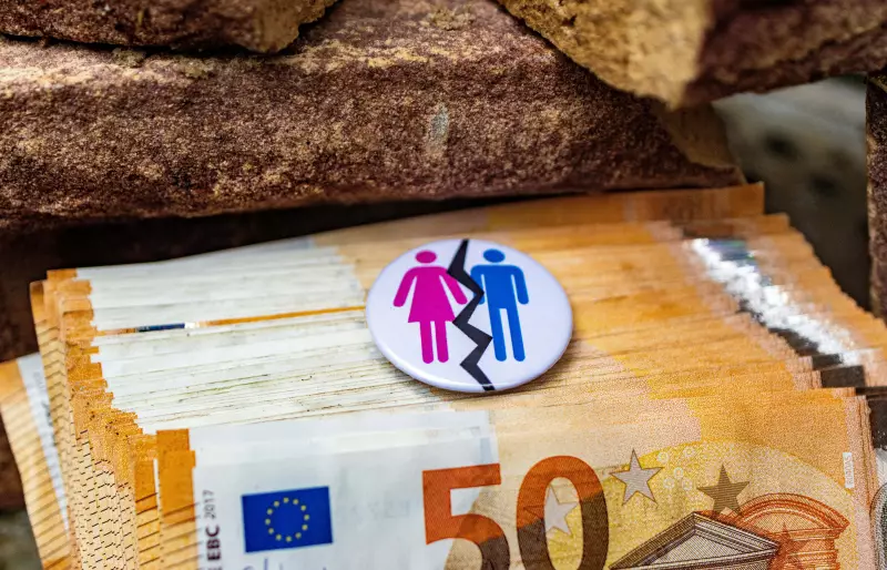 Mehrere 50€-Scheine liegen auf einem Haufen, darauf liegt ein Ansteck-Button, auf dem Piktogramme einer Frau und eines Mannes zu sehen sind, durch die Piktogramme geht eine gezackte schwarze Linie Mehrere 50€-Scheine liegen auf einem Haufen, darauf liegt ein Ansteck-Button, auf dem Piktogramme einer Frau und eines Mannes zu sehen sind, durch die Piktogramme geht eine gezackte schwarze Linie