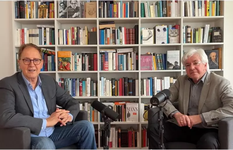 Michael Opielka und Frank Nullmeier sitzen vor einem Bücherregal und zeichnen die Podcastfolge auf. Vor ihnen stehen zwei große Mikrofone.