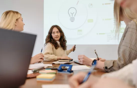 Mehrere Personen sitzen an einem Tisch und diskutieren. Im Hintergrund ist eine Präsentation zu sehen. Mehrere Personen sitzen an einem Tisch und diskutieren. Im Hintergrund ist eine Präsentation zu sehen.