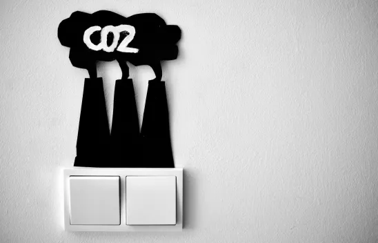 Zwei Lichtschalter nebeneinander. Darüber sind aus Papier drei Kraftwerktürme, die eine Wolke produzieren, in der "CO2" steht. Zwei Lichtschalter nebeneinander. Darüber sind aus Papier drei Kraftwerktürme, die eine Wolke produzieren, in der "CO2" steht.