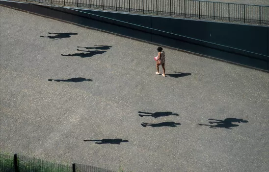 Person auf grauem Asphalt gehend. Ringsherum mehrere menschliche Schatten, zu denen aber keine Personen sichtbar sind. Person auf grauem Asphalt gehend. Ringsherum mehrere menschliche Schatten, zu denen aber keine Personen sichtbar sind.