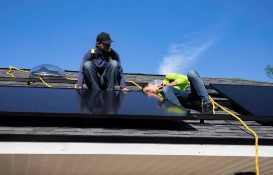 Zwie Personen arbeiten an einem Solarpanel auf dem Dach eines Hauses Zwie Personen arbeiten an einem Solarpanel auf dem Dach eines Hauses