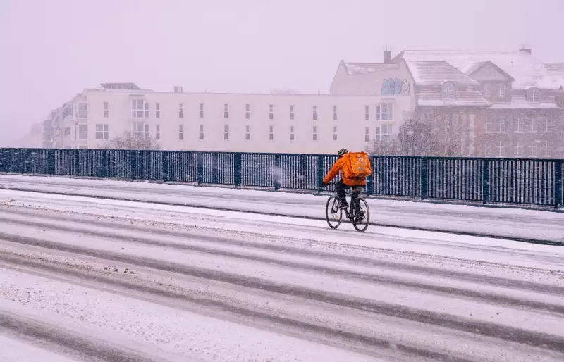 Ein Fahrradkurier in orangefarbener Kleidung fährt auf einem Fahrrad, die Fahrbahn ist verschneit.