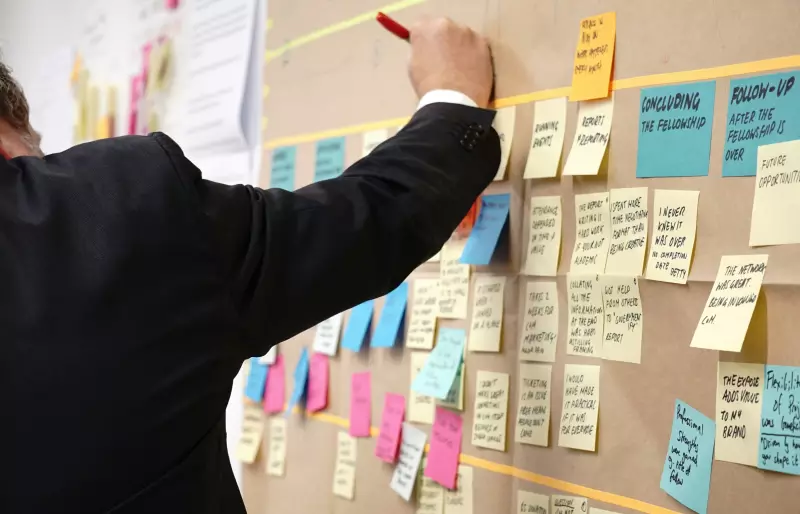 Eine Person steht vor einem Whiteboard, an dem mehrere Post-Its befestigt sind und schreibt etwas auf.