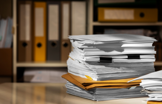 Ein Stapel Dokumente liegt auf einem Tisch vor einem Schrank mit Aktenordnern
