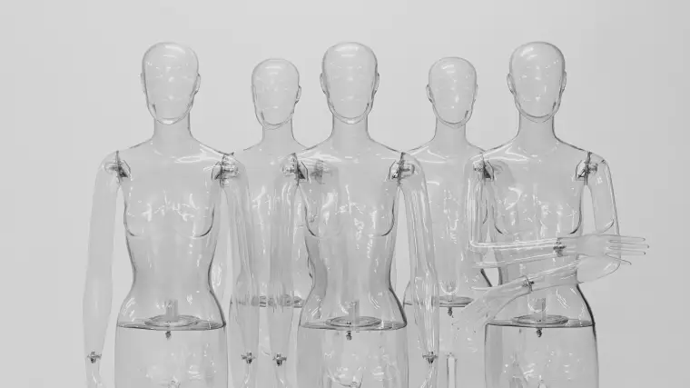 Transparente Schaufensterpuppen stehen vor einer weißen Wand.