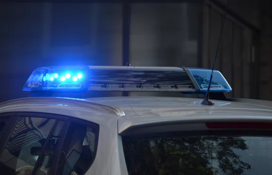 Der Ausschnitt eines Polizeiautos, auf dessen Dach Blaulicht leuchtet. 