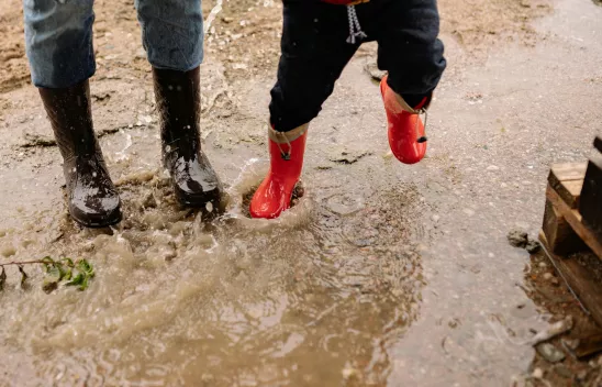 Beine zweier Personen, eine erwachsen, eine im Kindesalter, mit Gummistiefeln bekleidet in einer Pfütze springend. Beine zweier Personen, eine erwachsen, eine im Kindesalter, mit Gummistiefeln bekleidet in einer Pfütze springend.