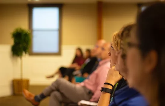 Mehrere Personen, die in einem Raum sitzen und einem Vortrag folgen Mehrere Personen, die in einem Raum sitzen und einem Vortrag folgen