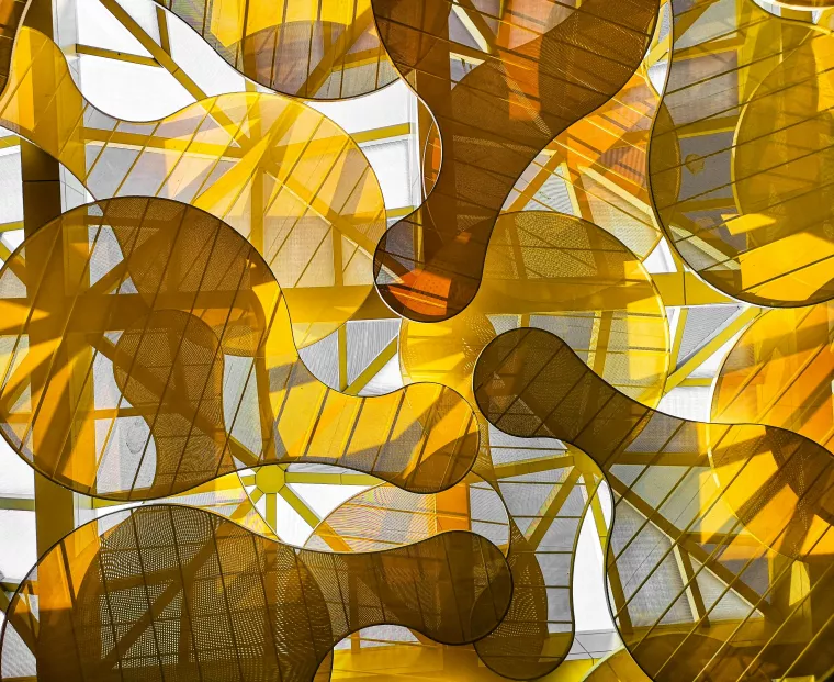 Mit transparentem, gelben Stoff bespannte organische Figuren vor einer Glaswand.