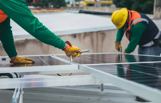 Zwei Personen in Arbeitskleidung arbeiten mit Werkzeug an Solarpanels Zwei Personen in Arbeitskleidung arbeiten mit Werkzeug an Solarpanels