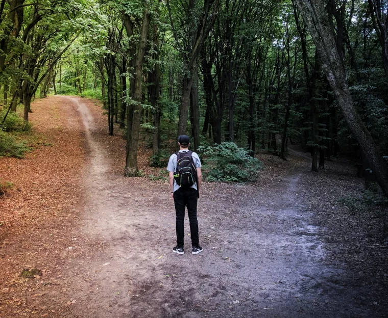 Jugendlicher steht an einer Weggabelung im Wald.